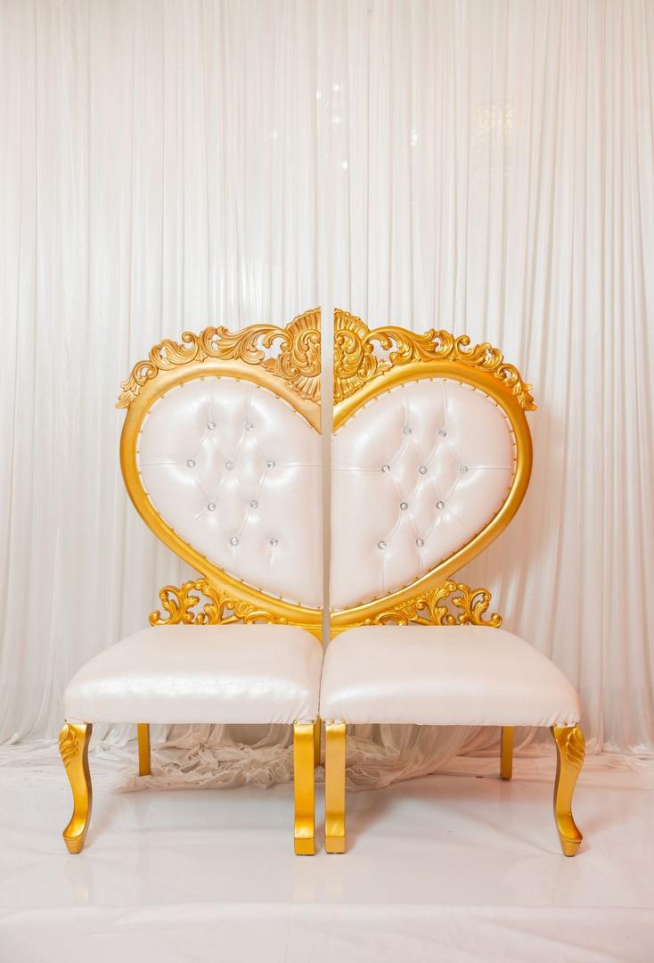 A gold and white heart shaped chair in front of a curtain.