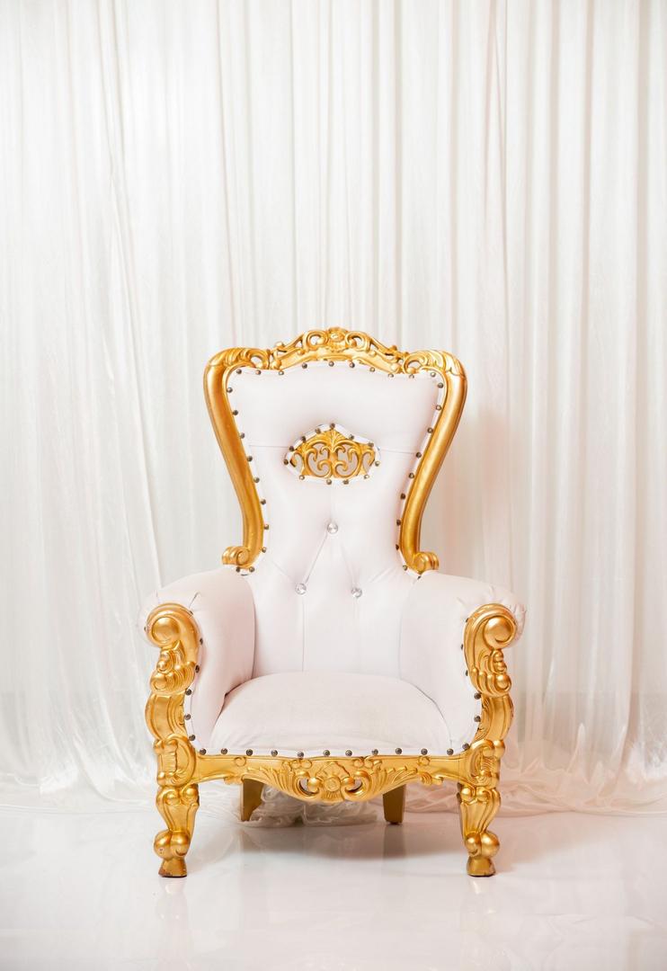 A white and gold chair with a white curtain behind it.