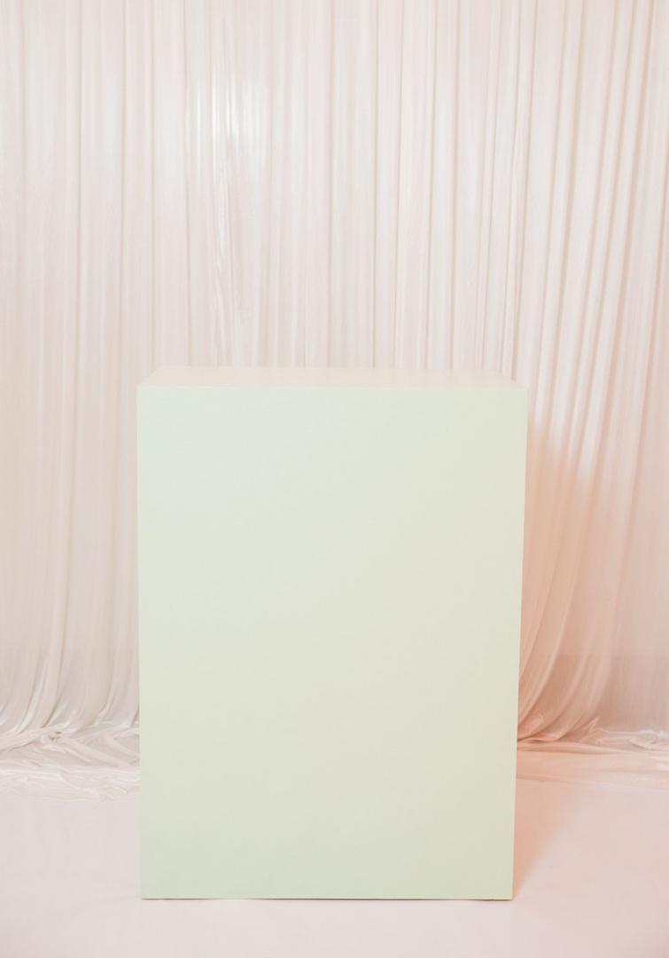 A white pedestal with a curtain behind it.