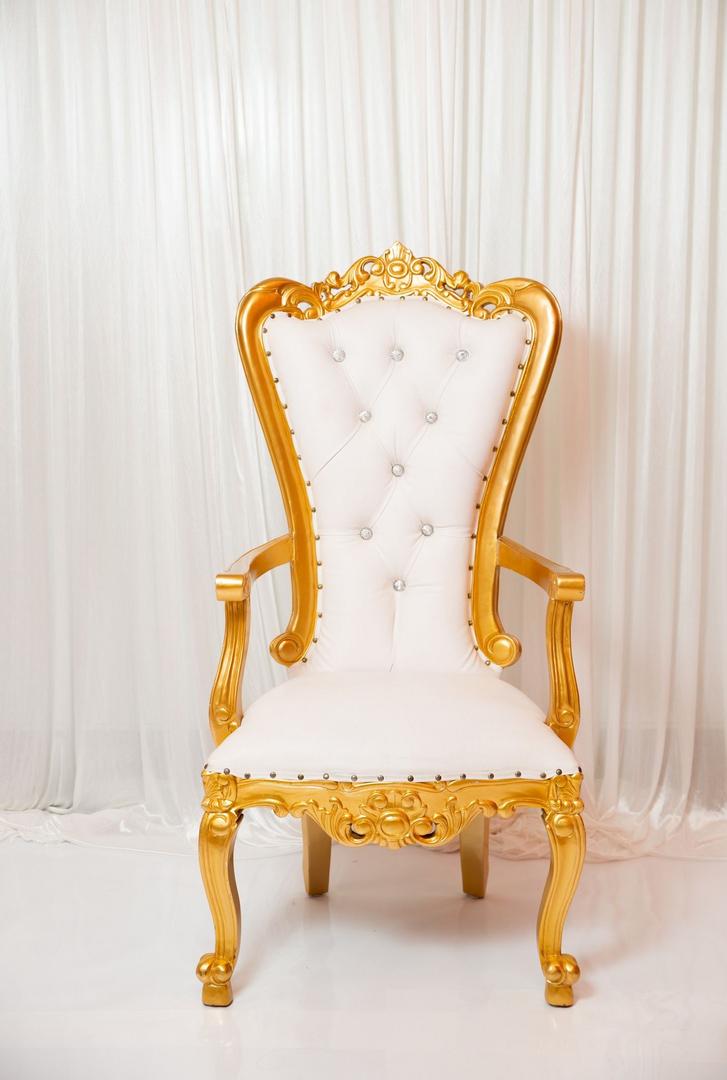 A white and gold chair with a white curtain behind it.