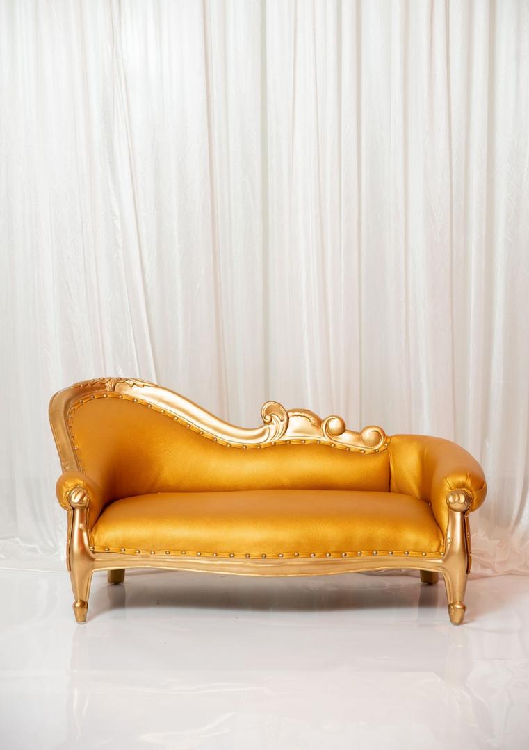 A gold couch with a white curtain behind it