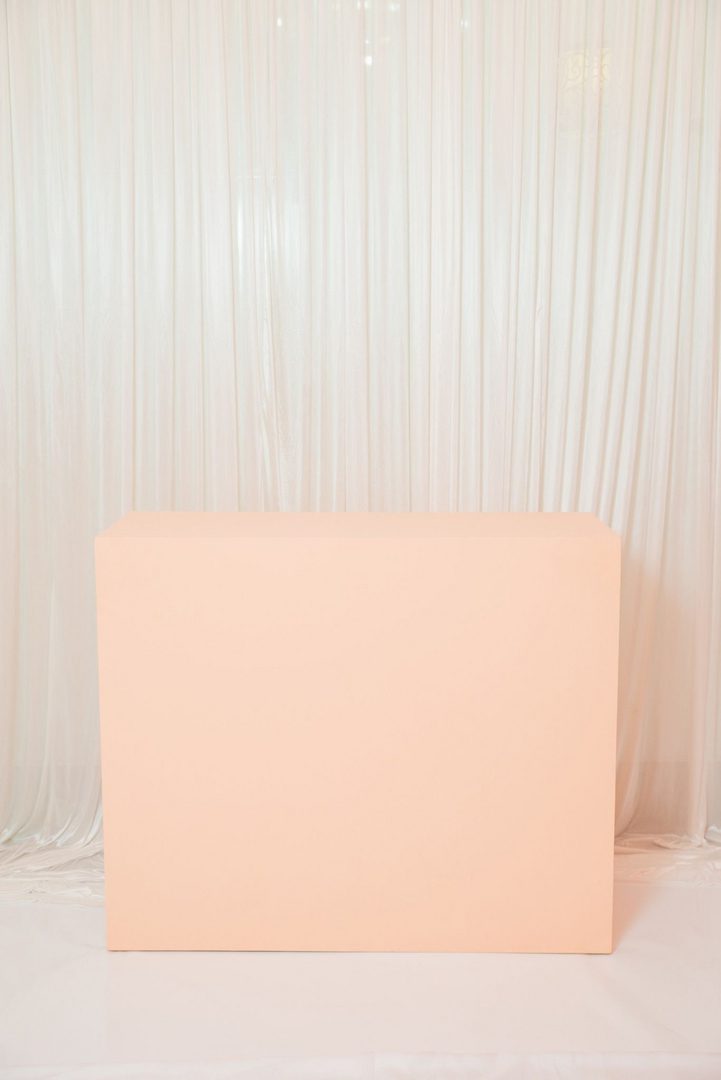 A pink box sitting in front of white curtains.