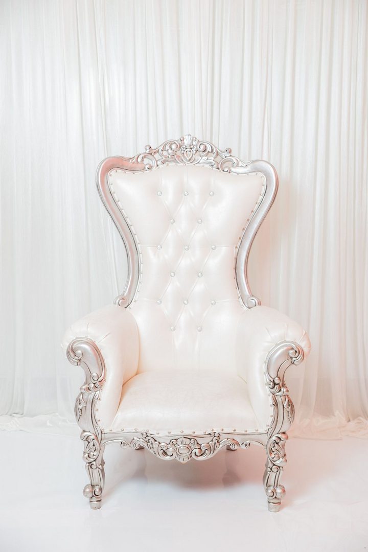 A white chair with silver trim and tufted back.